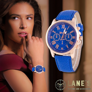 dark blue faced watch with roman numeral numbers which are gold with a gold trim and a blue strap on a woman's wrist