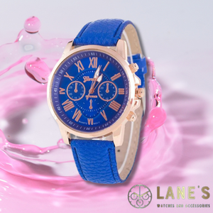 dark blue faced watch with roman numeral numbers which are gold with a gold trim and a blue strap on a pink background