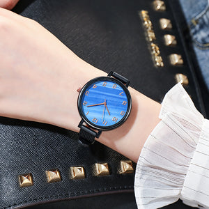 blue faced watch with gold numbers and a black trim with a black strap on a woman's wrist