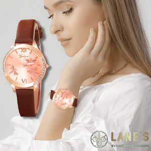 rose gold face watch with 3 dragonflies on it with roman numeral number 12 and 6. with a rose gold trim with  crystals on either side and an elegant brown strap on a woman's wrist