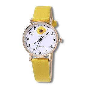 white faced watch with black numbers and a yellow sunflower at the top with black hands and a gold trim with a yellow strap