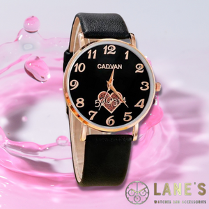 black faced watch with gold numbers and a glittery heart below the centre with a gold trim and a black strap on pink background