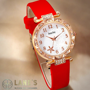 white faced watch with gold numbers and a gold trim with crystals and a red strap on a beige background